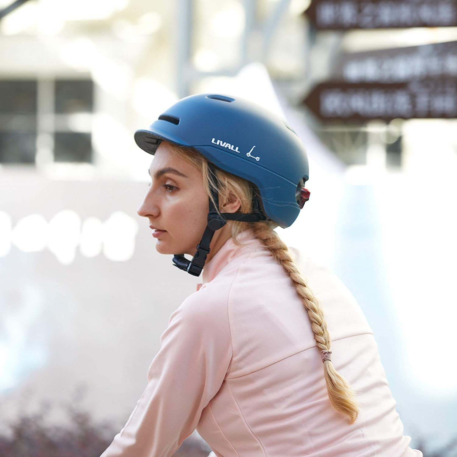 Mujer con casco azul y chaqueta rosa, montando en bicicleta. Fondo borroso.