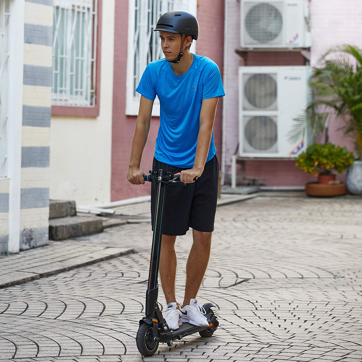 Hombre en un scooter eléctrico negro, en una calle pavimentada con edificios.