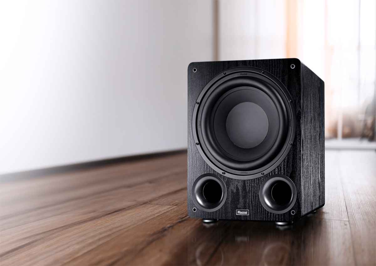 Schwarzer Subwoofer auf Holzboden, weißer Wandhintergrund. Zwei nach vorne gerichtete Ports.