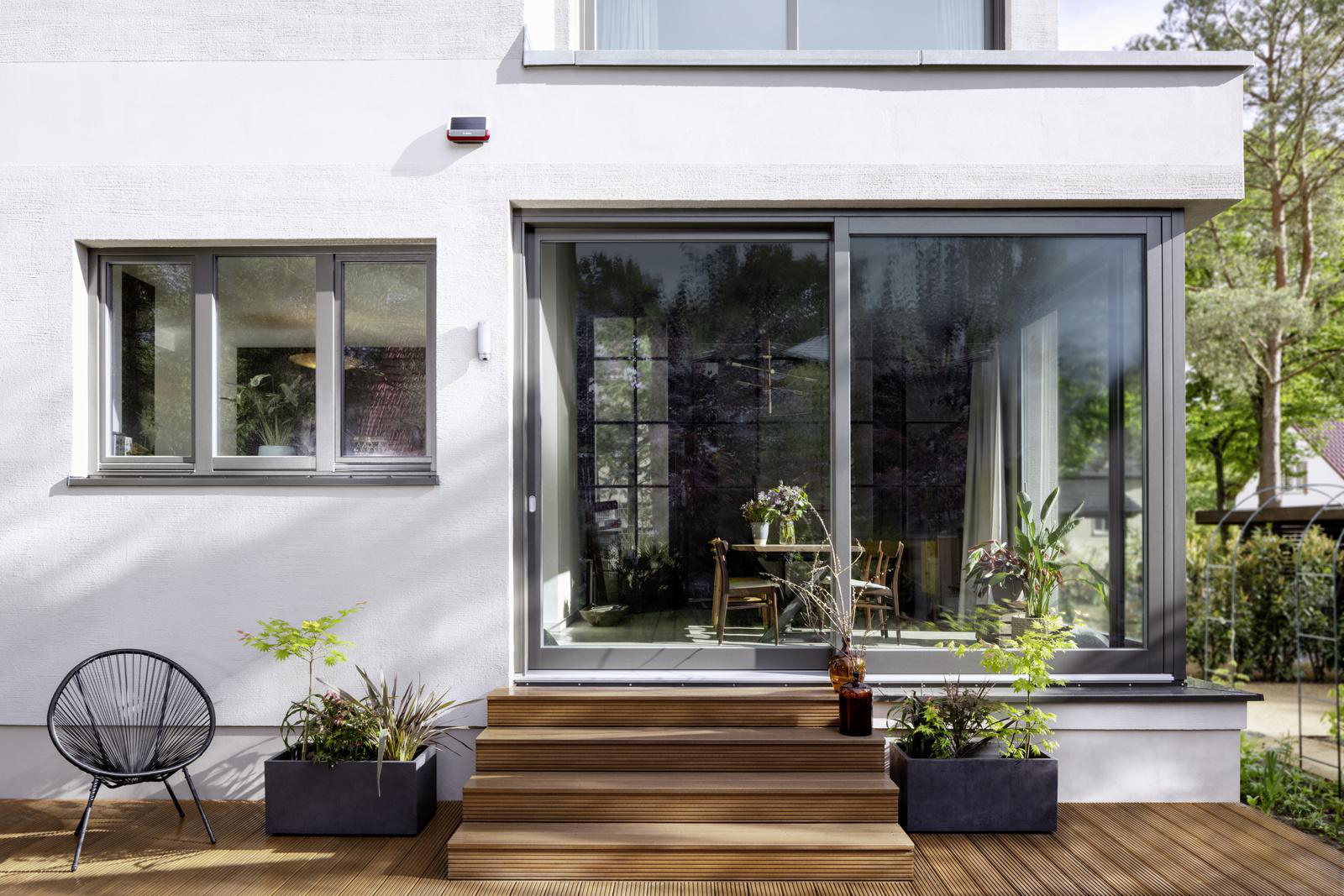 Modernes Hausäußeres mit Holzterrasse, Glasschiebetüren und Landschaftsgestaltung.