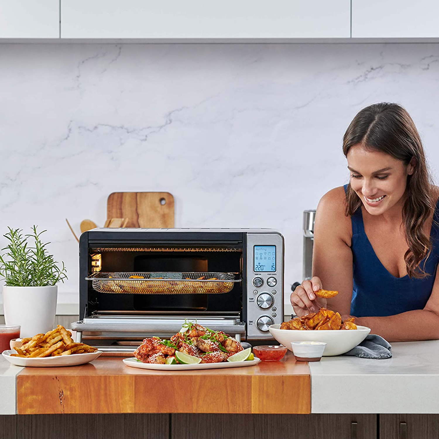 Una donna con un top blu sorride a un tavolo con cibo e un forno.