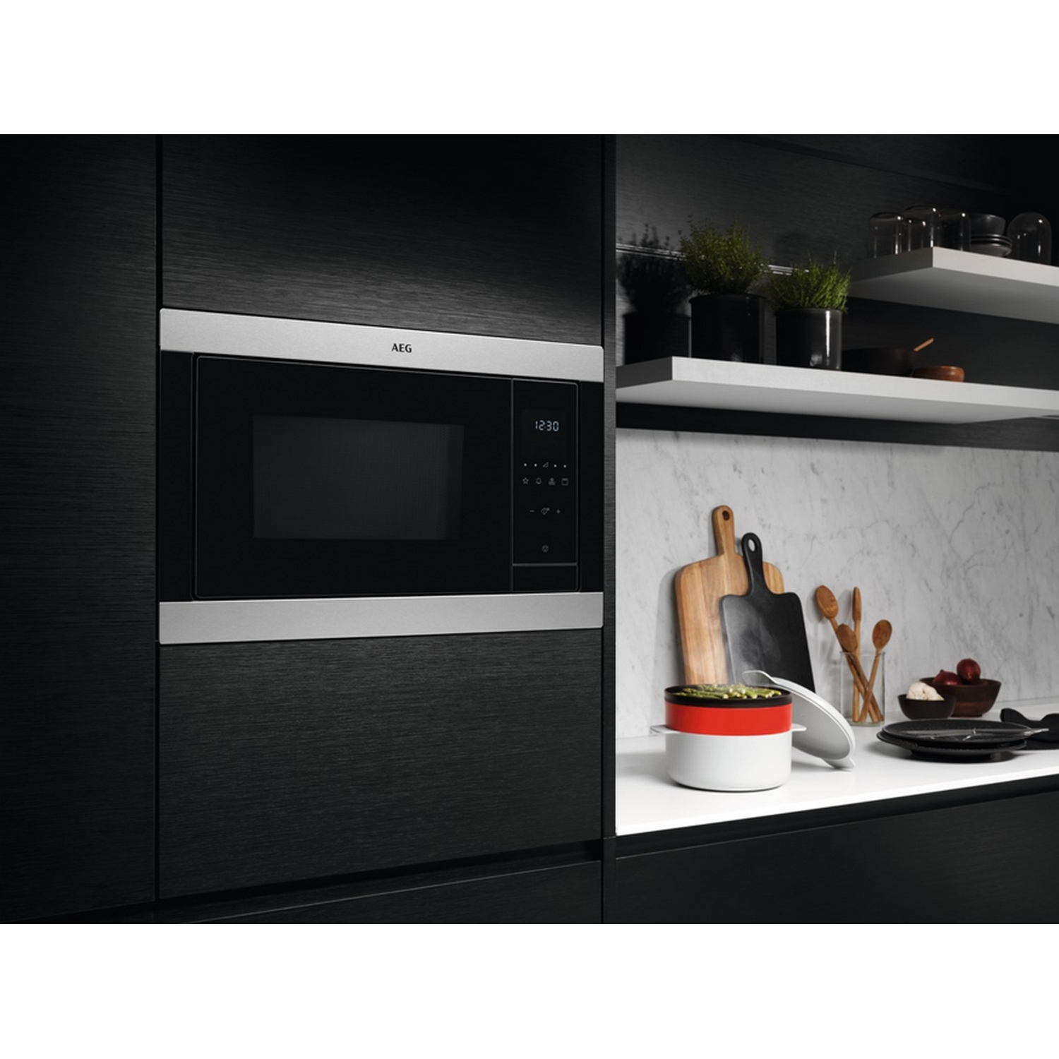 Horno microondas en un entorno de cocina negro con varios utensilios de cocina.