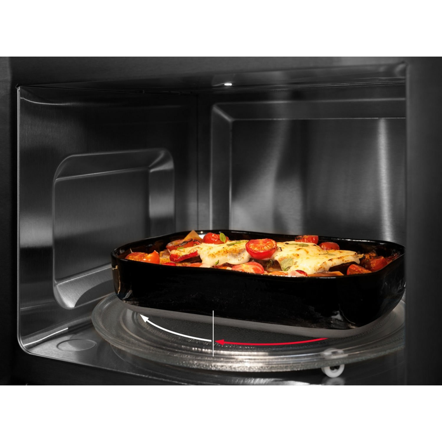 Interior de un microondas con un plato negro que contiene comida. El plato de vidrio está girando dentro del microondas.
