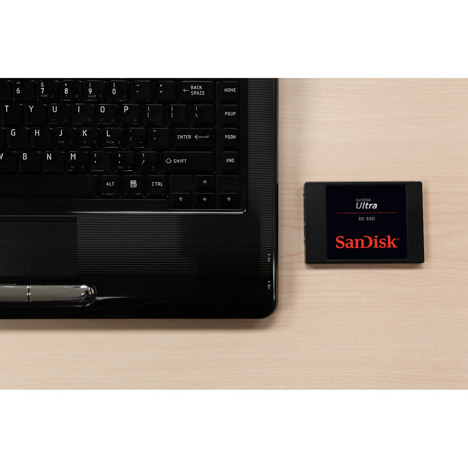 Teclado de portátil y SSD Sandisk Ultra en un escritorio de madera. SSD es negro y rojo.