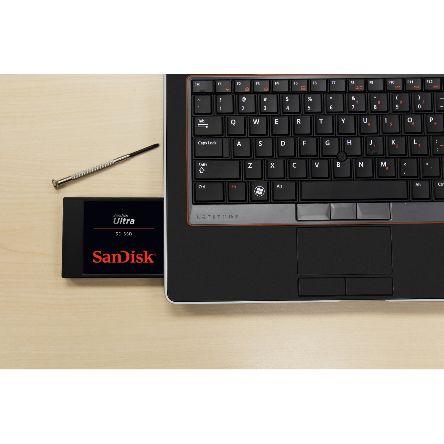 Teclado de portátil con SSD SanDisk sobre superficie de madera y destornillador.