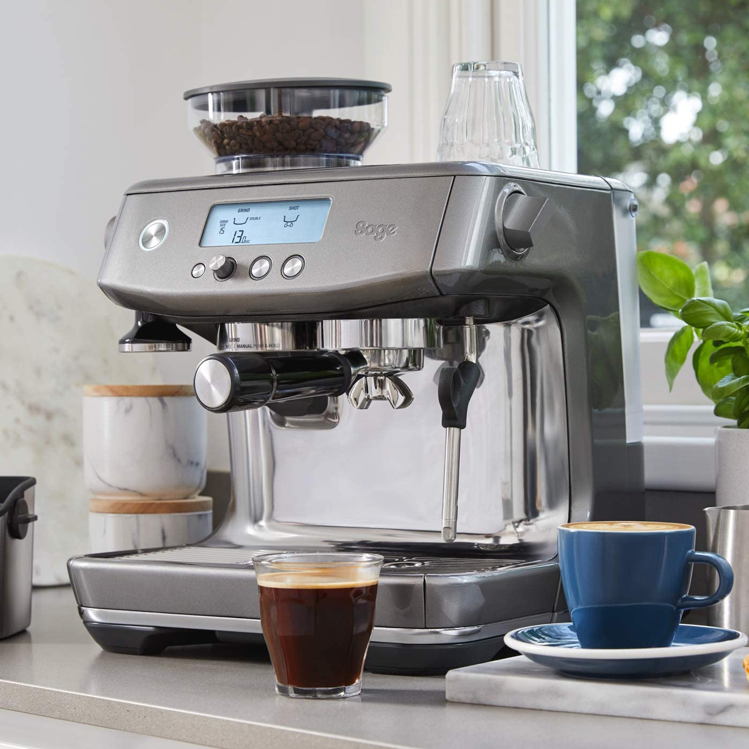 Macchina per espresso argentata con accessori: tazza da caffè, bicchiere e macinacaffè con chicchi.