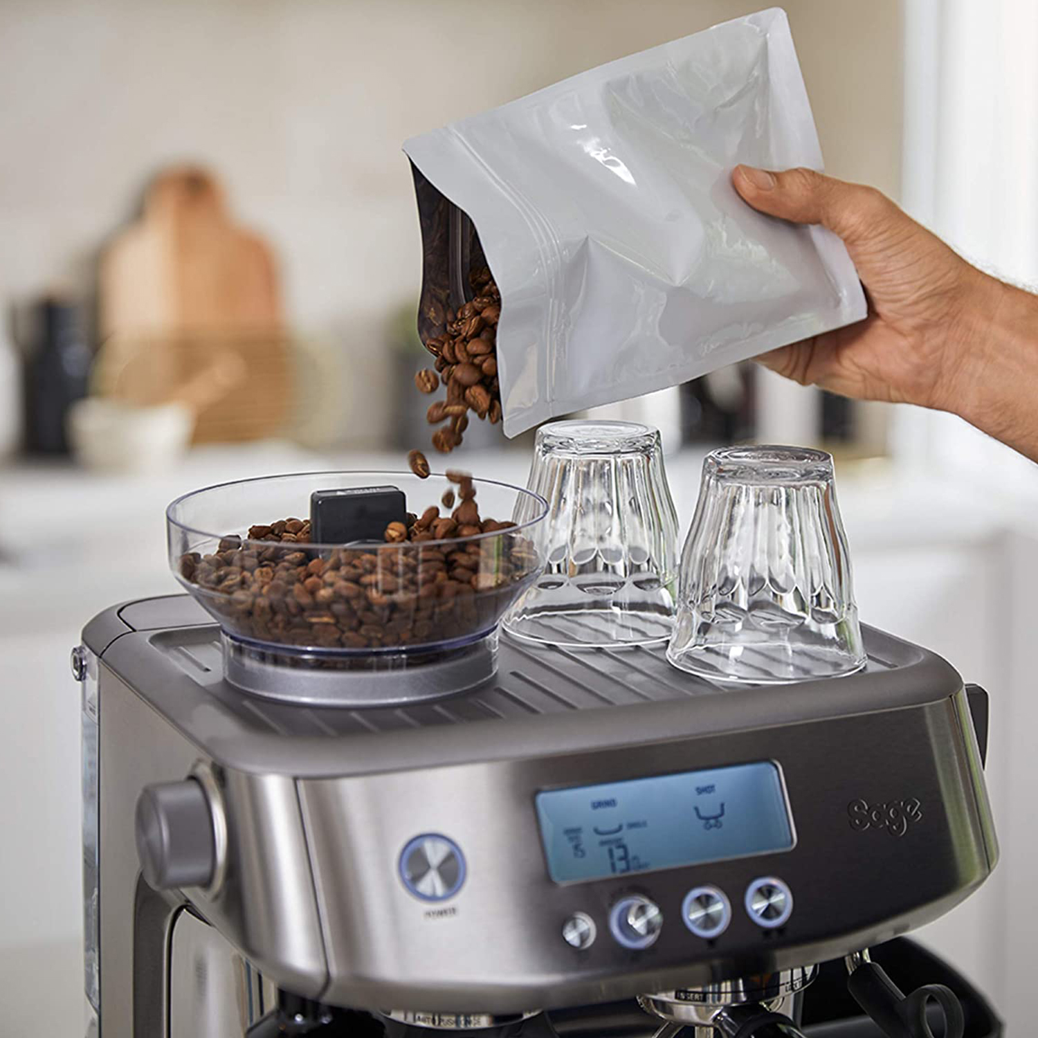 Persona versa chicchi di caffè in una ciotola sulla macchina per espresso. Due bicchieri dietro.