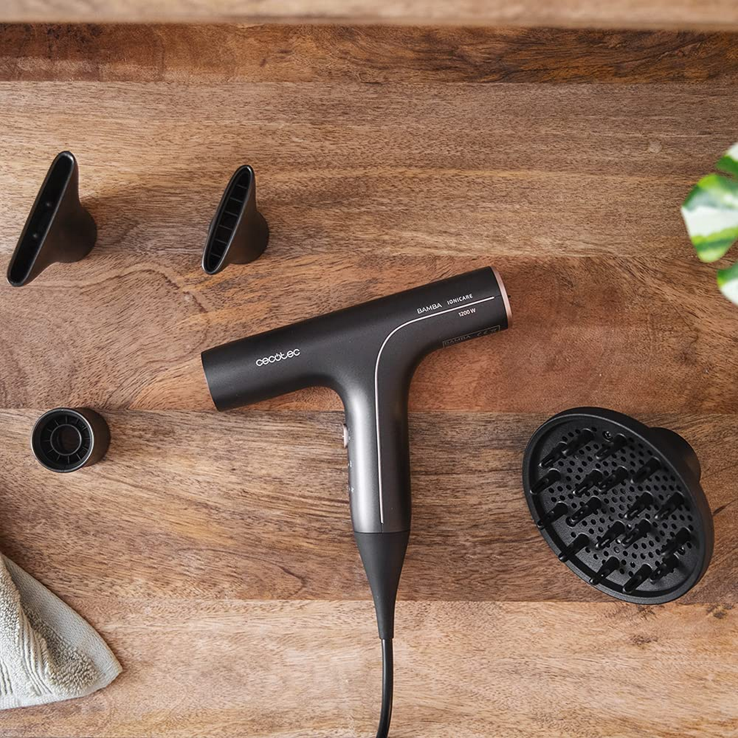 Un secador de pelo negro con accesorios sobre una mesa de madera. Los accesorios son negros y rosas.