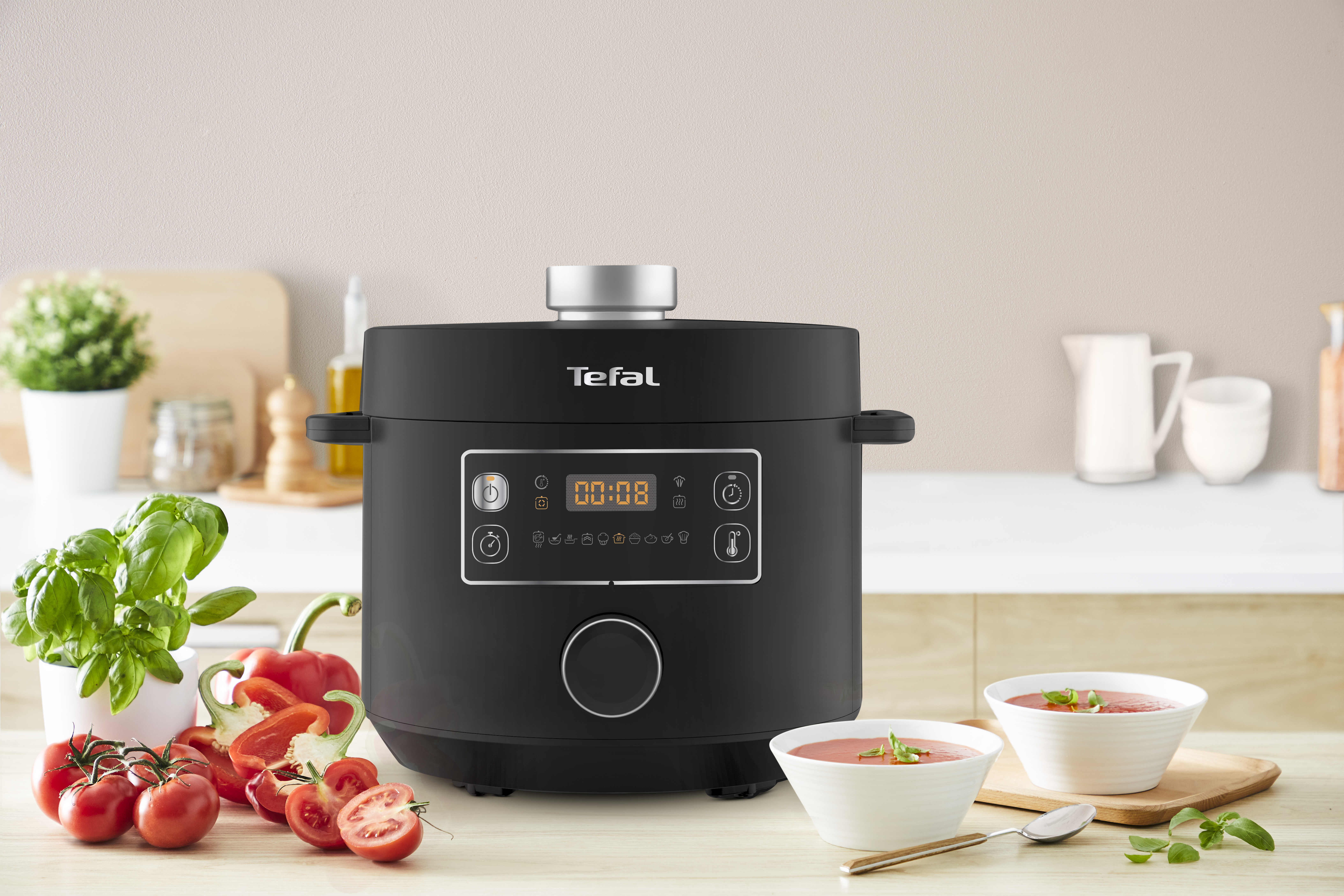 Fekete Tefal multicooker kijelzővel, paradicsommal és leveses tálakkal.