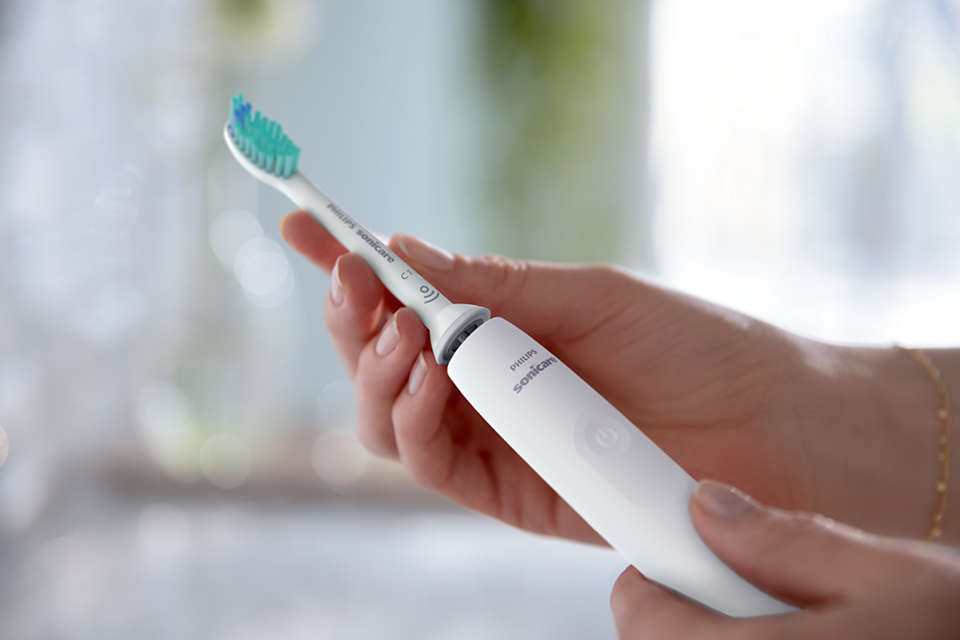 Egy személy egy fehér Philips Sonicare fogkefét tart. Homályos háttér. A fogkefe új.