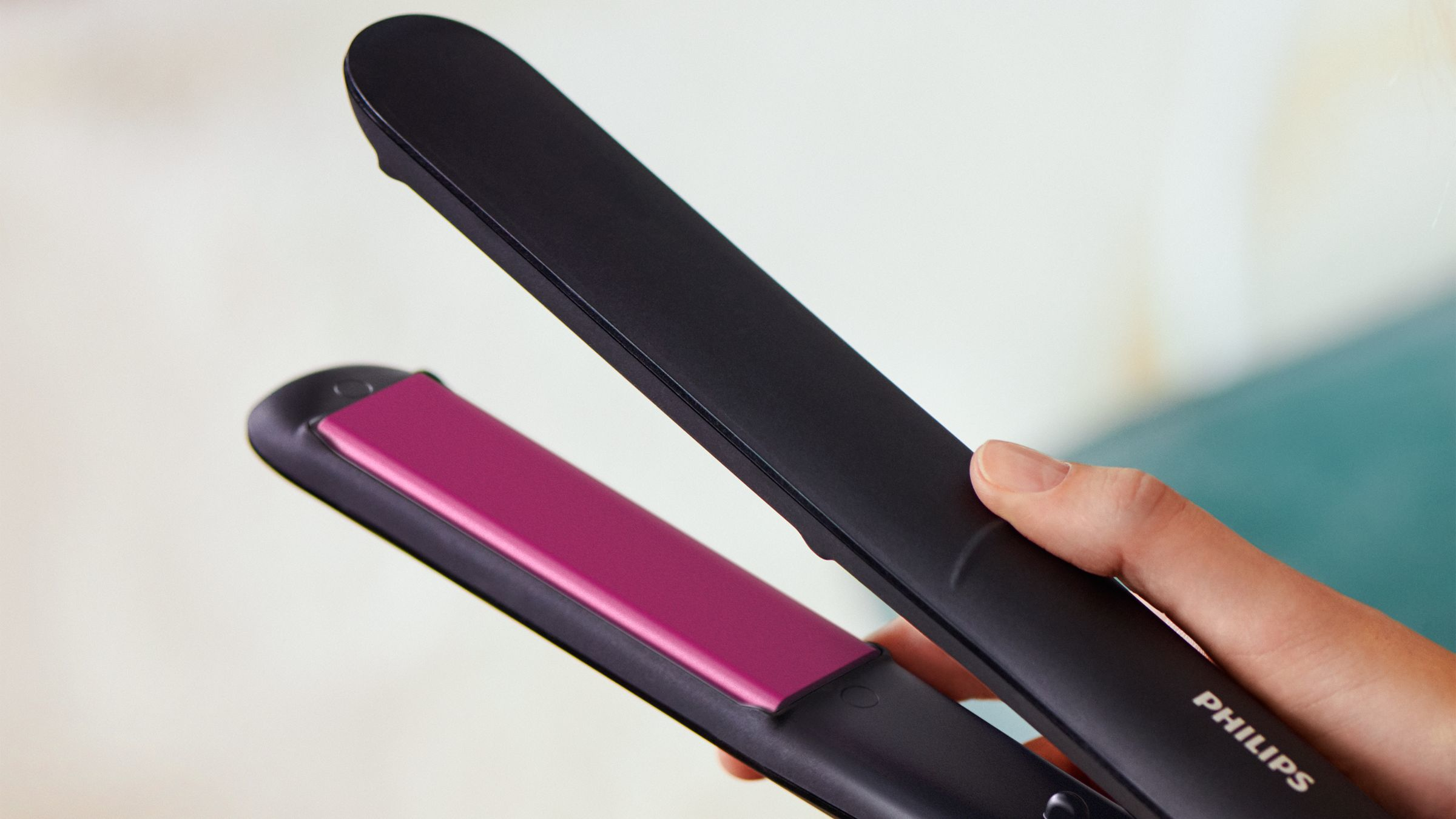 Plancha para el pelo negra con placa calefactora rosa, sostenida por una mano.