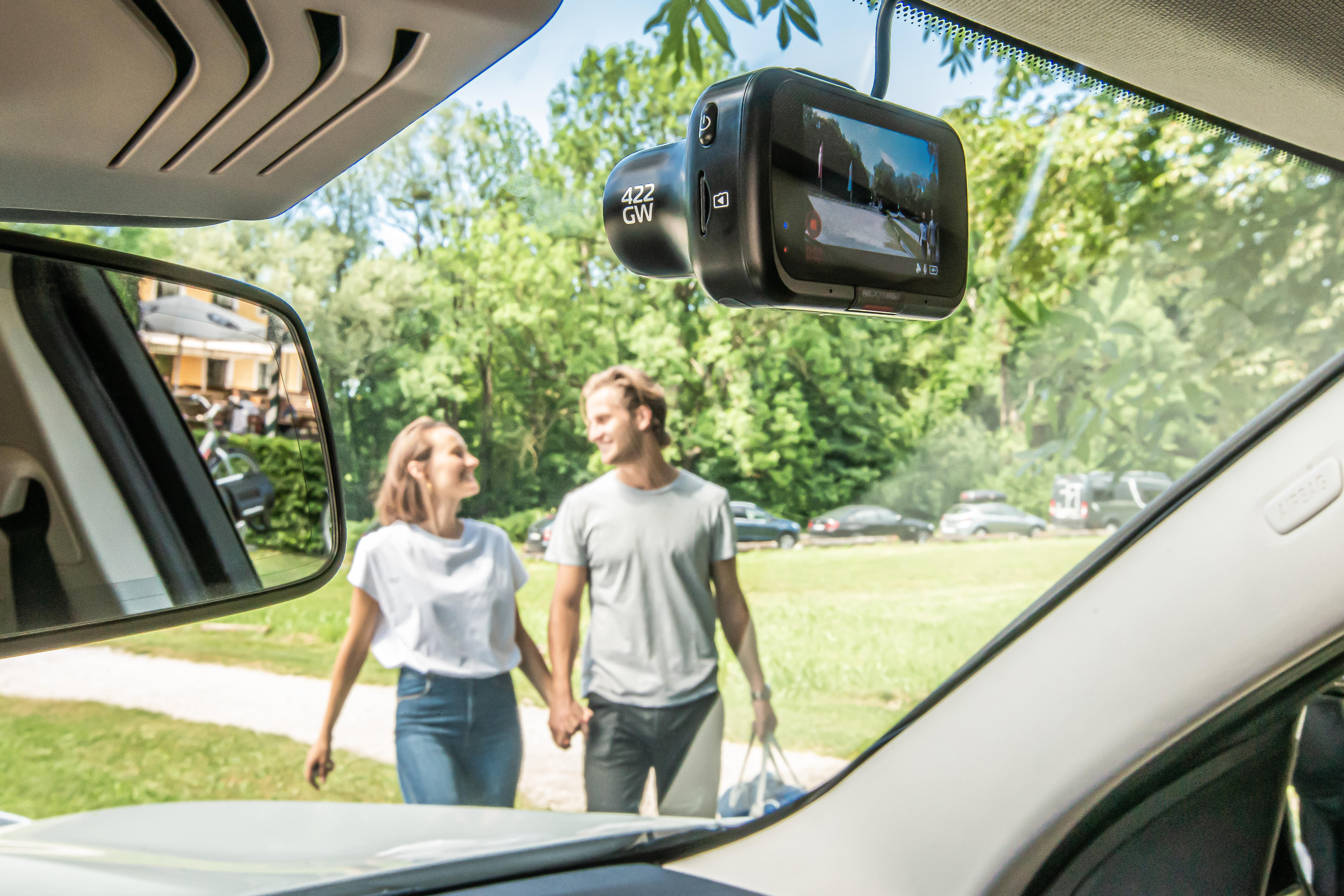 Paar geht Hand in Hand, mit Dashcam im Auto. Grüne Bäume und blauer Himmel im Hintergrund.