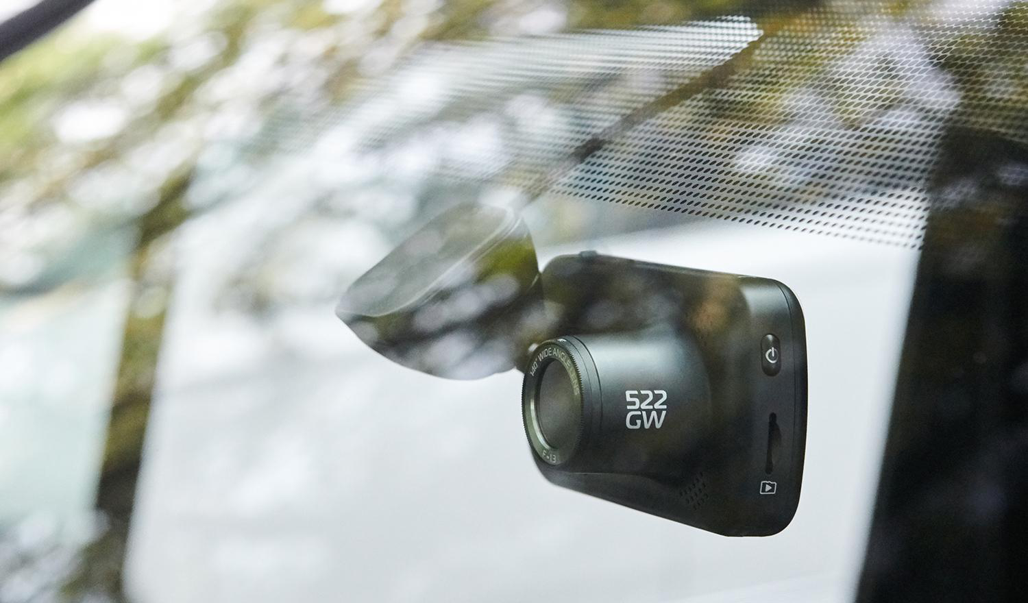 Ein schwarzer Dashcam an der Windschutzscheibe eines Autos, die Straße und unscharfer Hintergrund zeigend.