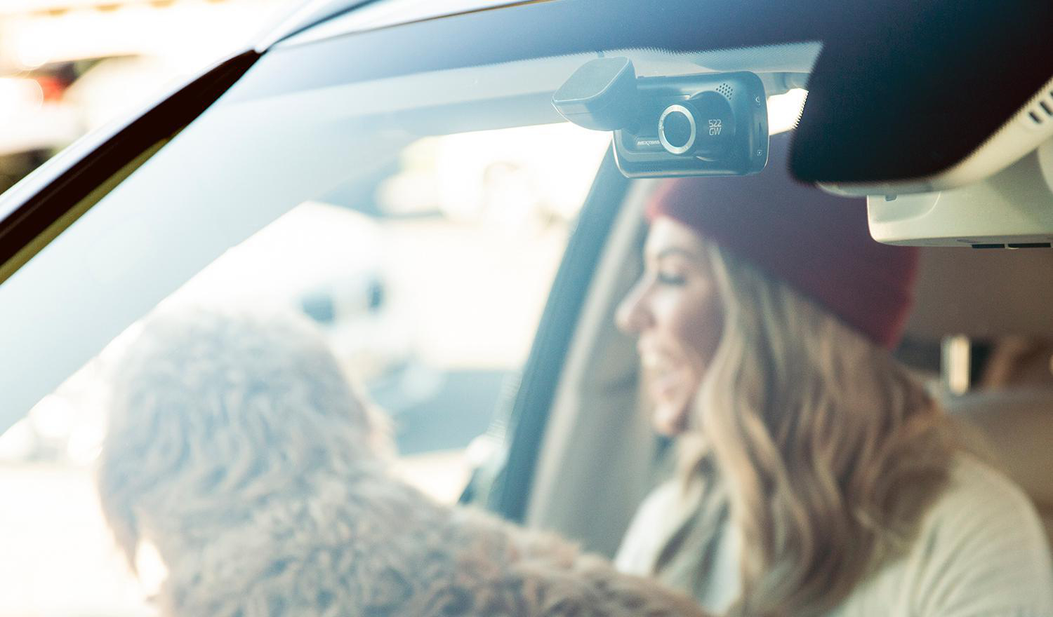 Eine Frau im Auto mit einer am Windschutzscheibe montierten Dashcam und einem Hund.
