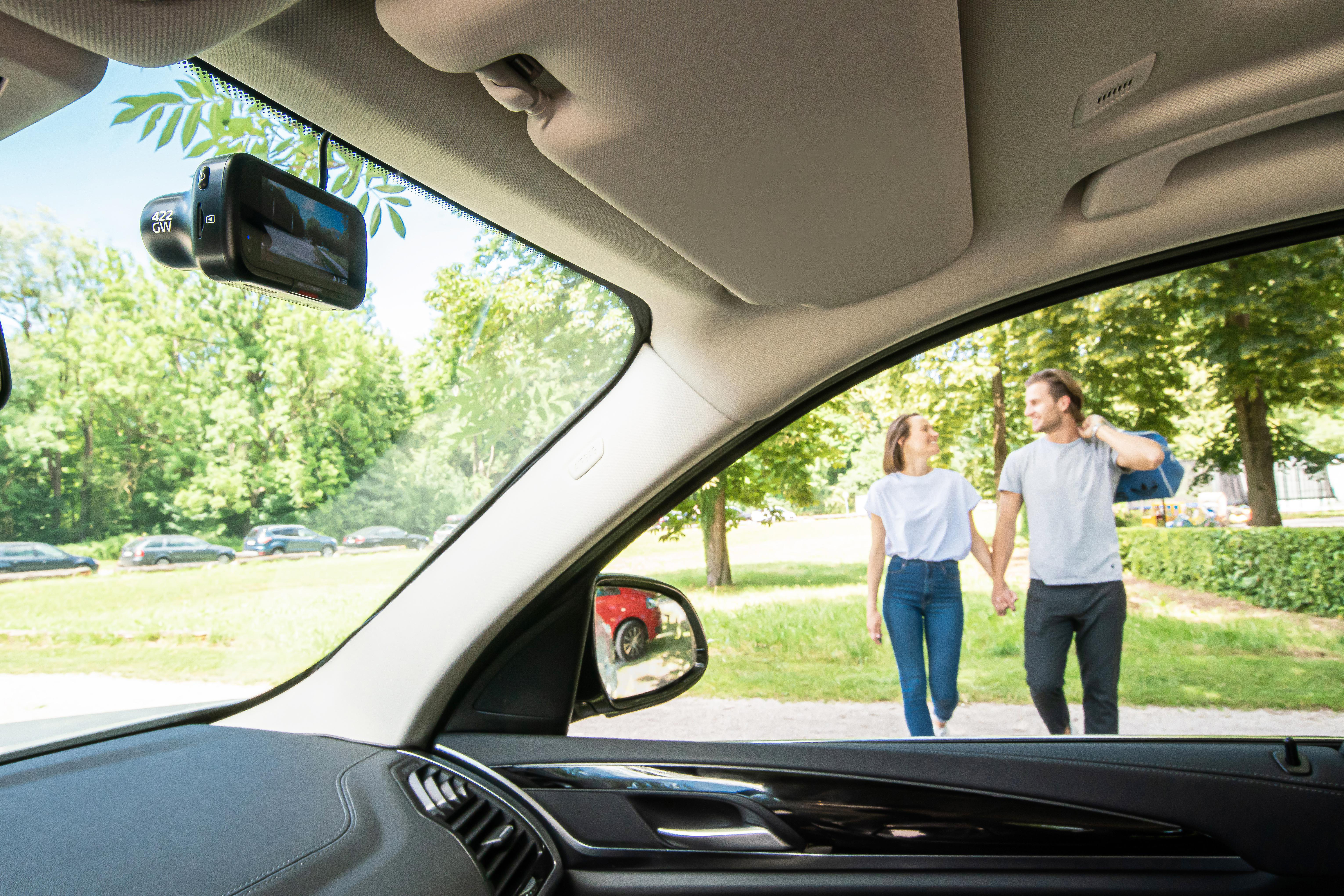 Im Auto: Dashcam, zwei Personen gehen, Bäume und Himmel sichtbar.