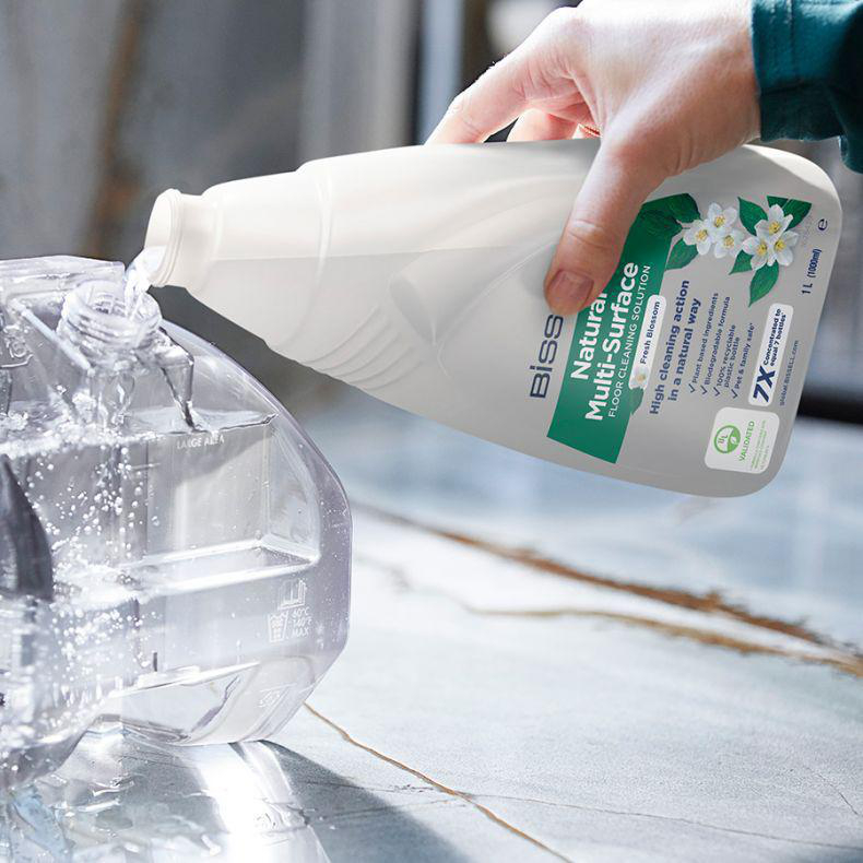 Hand gießt Reinigungslösung aus einer Flasche in einen transparenten Behälter.