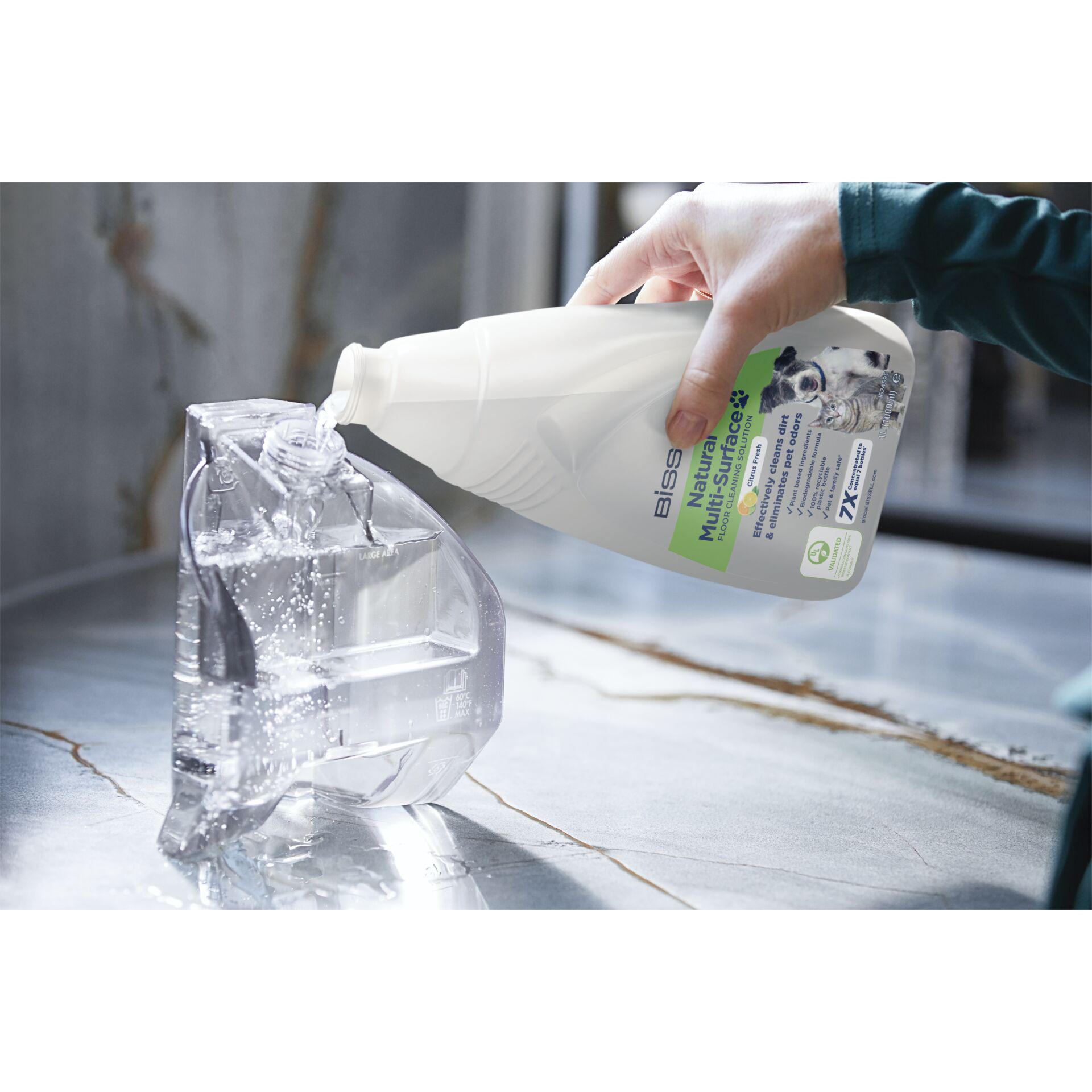 Hand gießt Reinigungslösung in einen transparenten Behälter. Der Behälter steht auf Marmor.