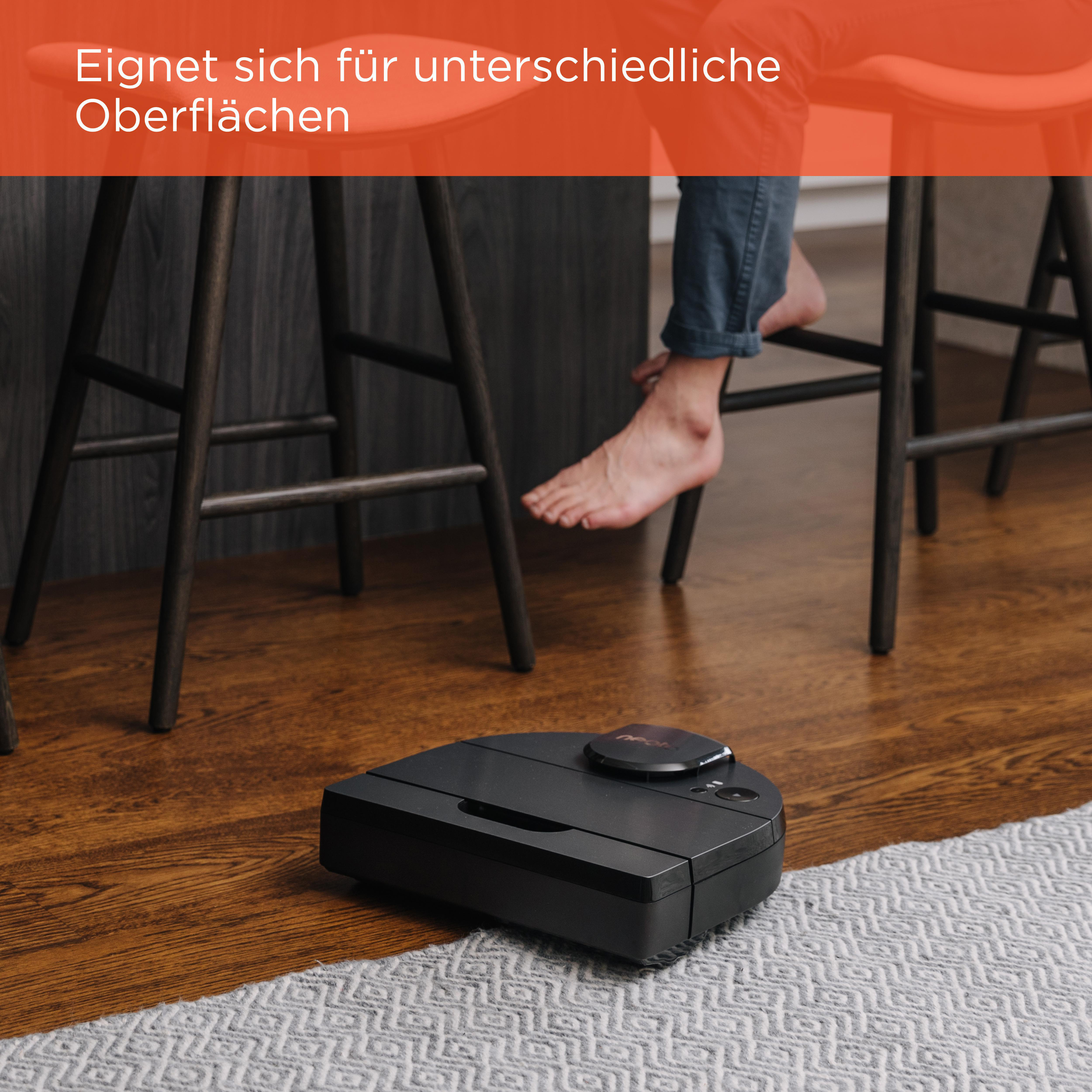Roboter-Staubsauger auf Holzboden, in der Nähe eines Teppichs und Füße einer Person.