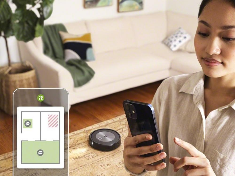 Vrouw houdt telefoon vast, toont robotstofzuiger en kaart op scherm, dichtbij de bank.