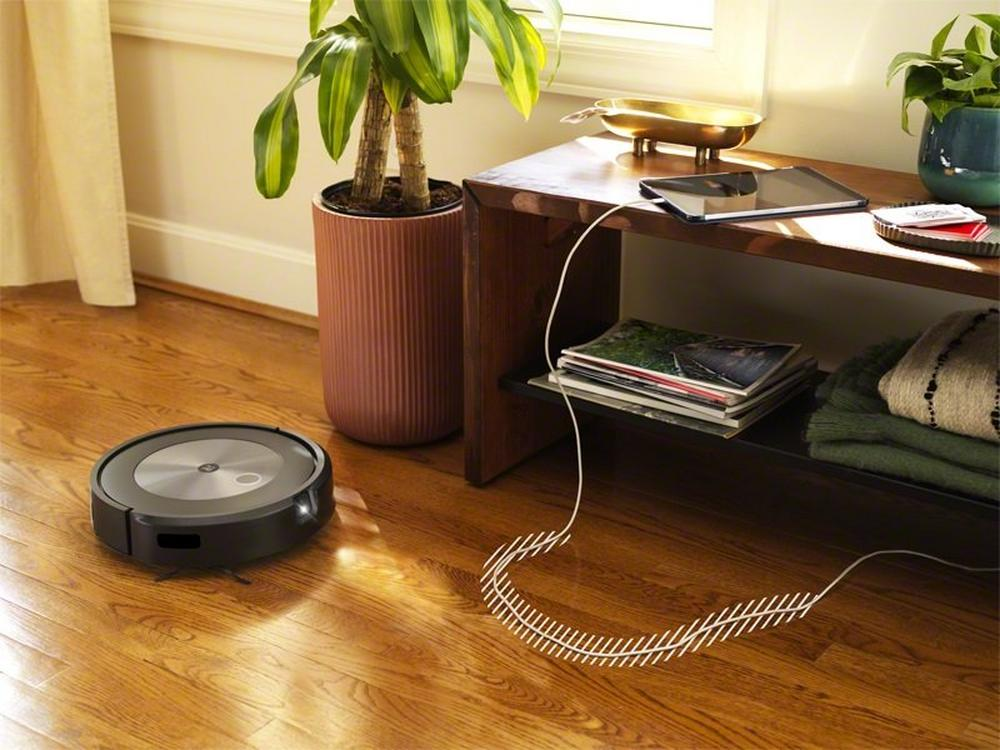 Een zwarte robotstofzuiger op een houten vloer naast een oplaadkabel.