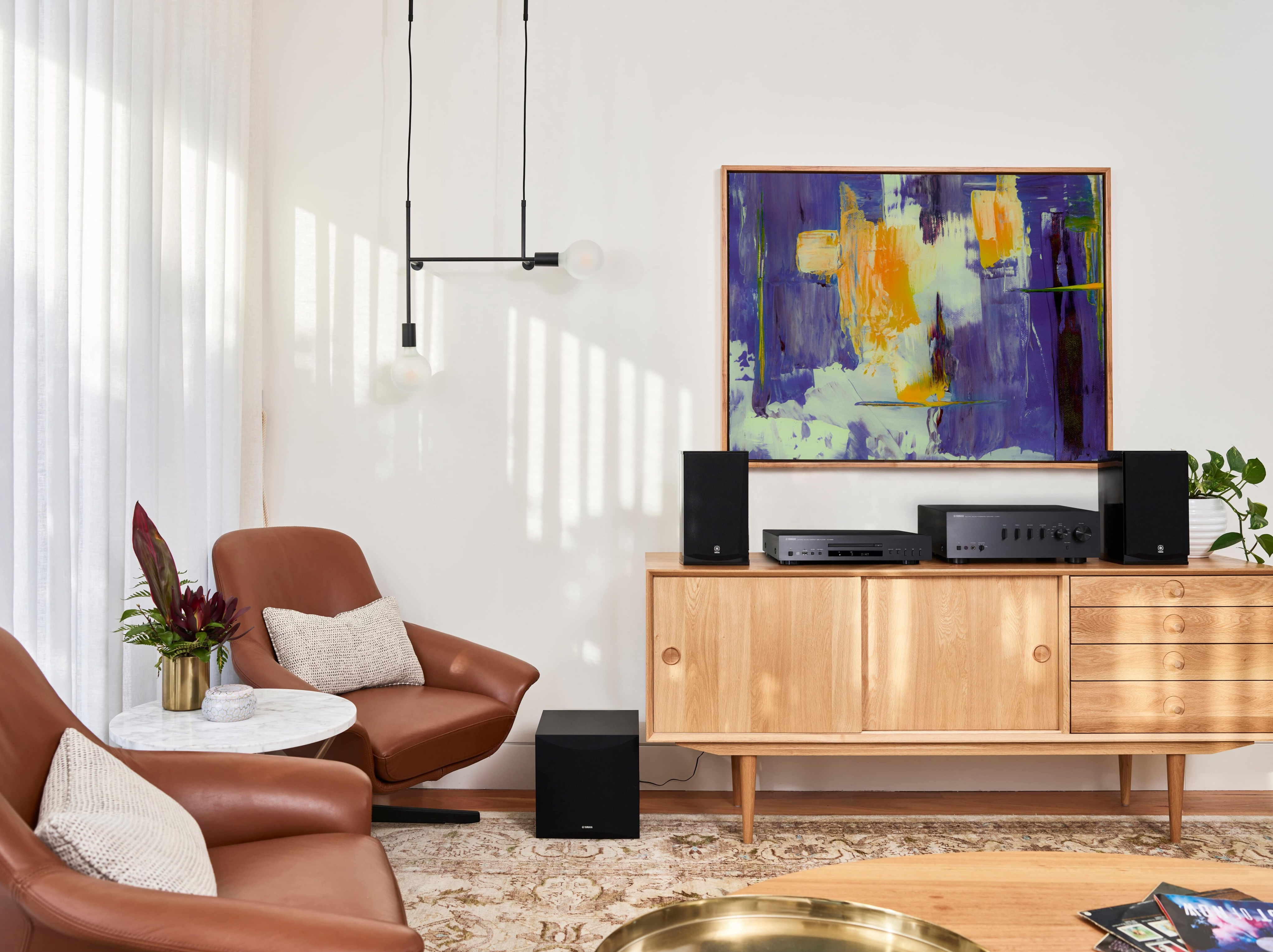 Wohnzimmer mit braunen Ledersesseln, Holzschrank, Kunstwerk und Soundsystem.