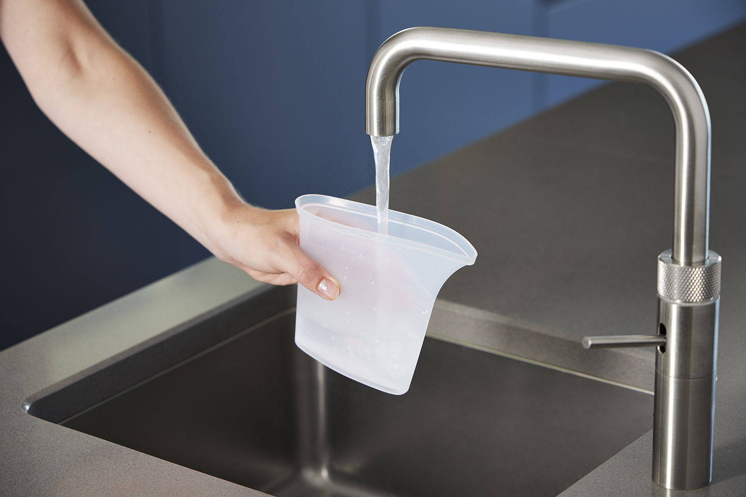Een hand houdt een maatbeker onder een metalen kraan, water giet erin.