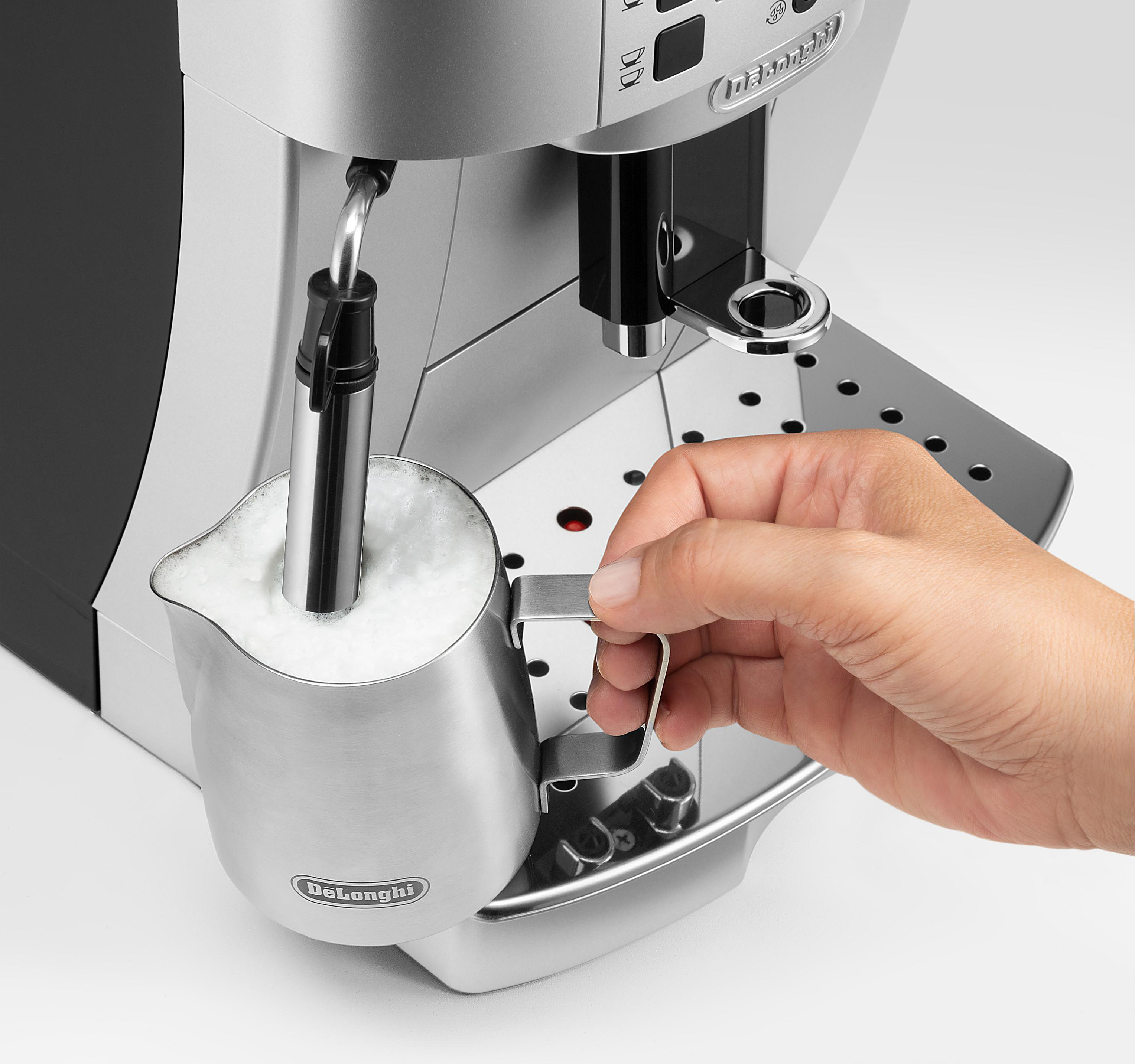 Eine Hand hält einen Milchaufschäumer neben einer silbernen Espressomaschine mit weißem Schaum im Krug.