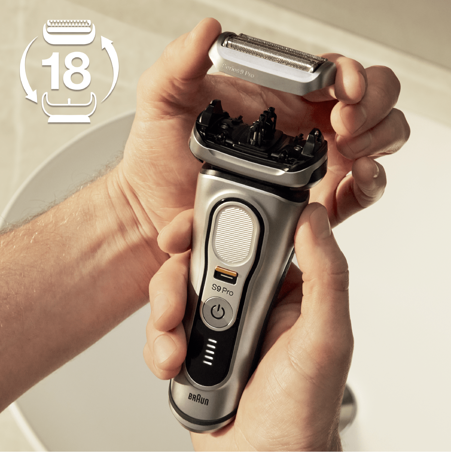 A man holding a shaver with its head detached. The shaver is silver and black, with a white background.