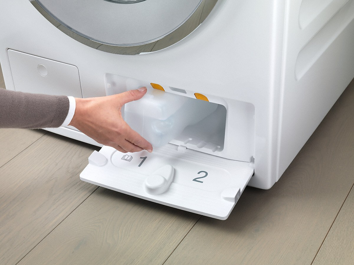 Una mano che rimuove un contenitore di detersivo da un cassetto bianco della lavatrice.