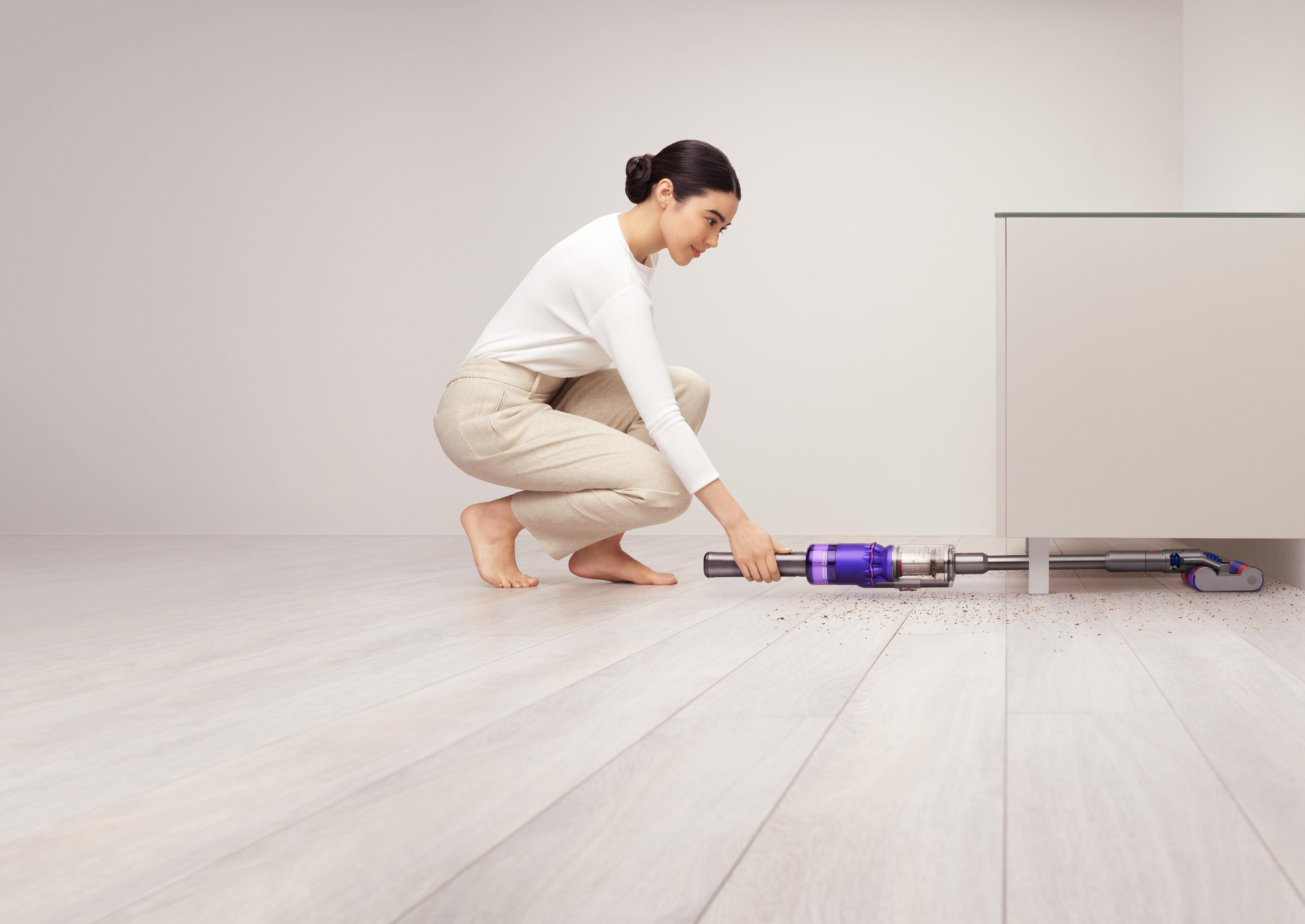 Eine Frau saugt den Boden mit einem lila-silbernen Staubsauger.