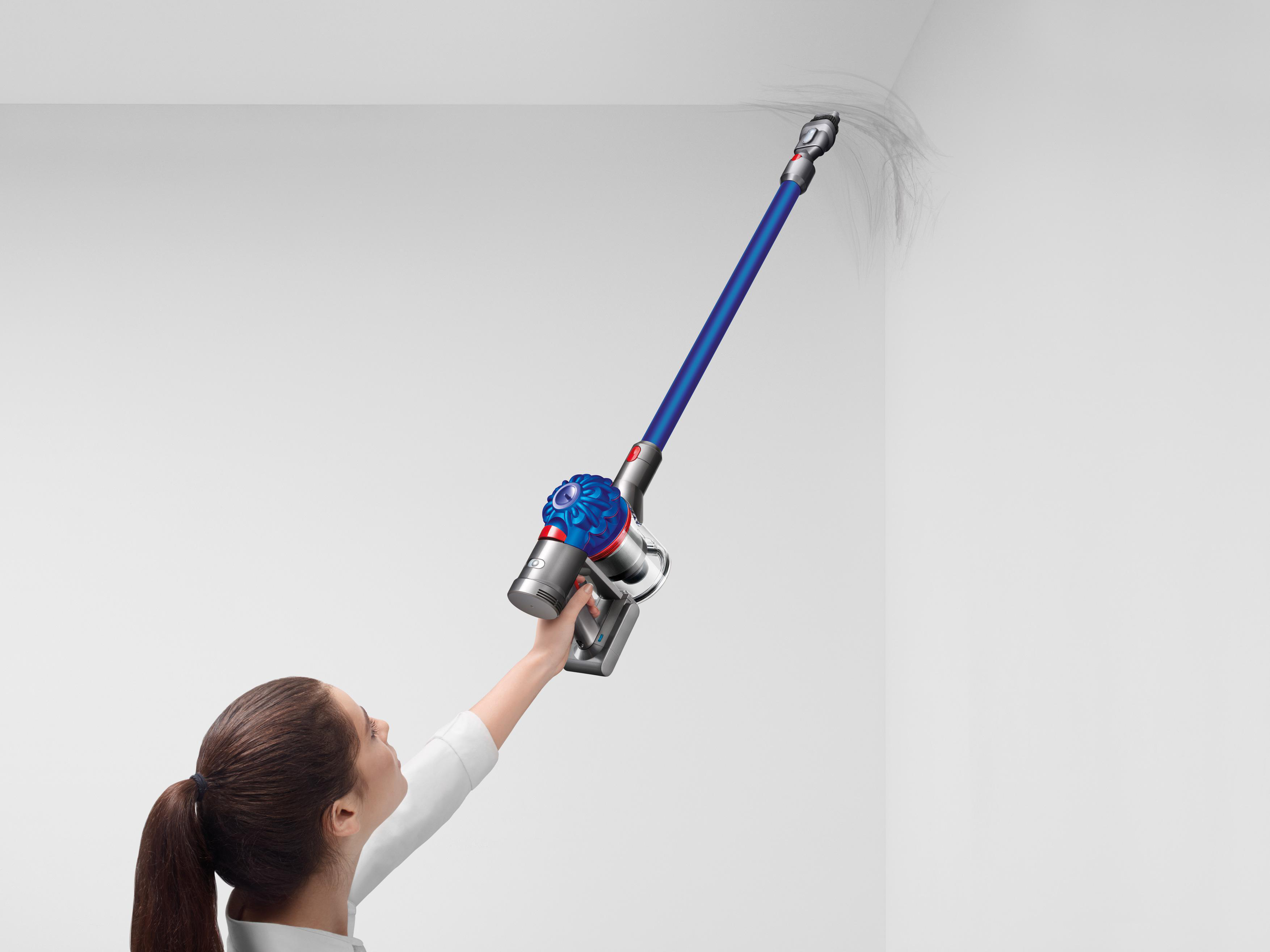 Frau, die einen blauen und silbernen Dyson-Staubsauger an einer weißen Wand benutzt.