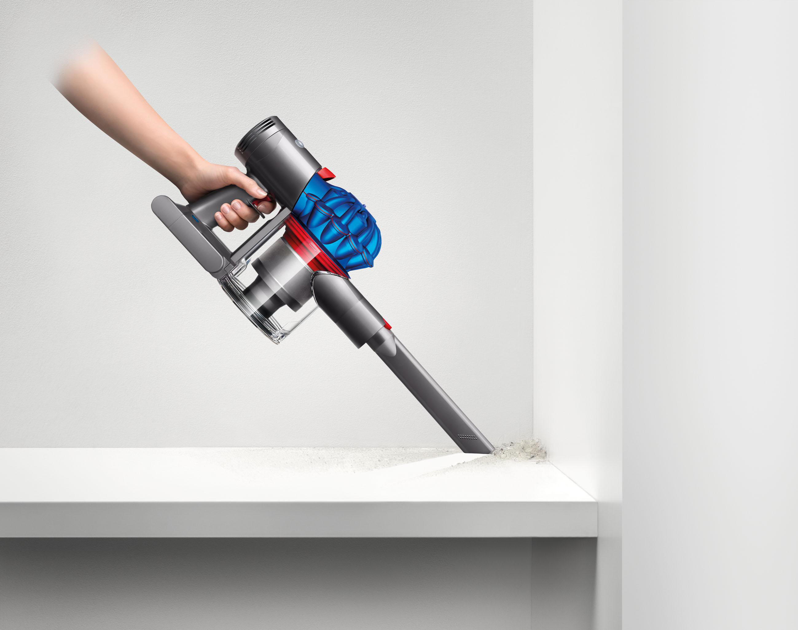 Eine Person, die einen grau-blauen Dyson-Staubsauger benutzt, um eine weiße Oberfläche zu reinigen.