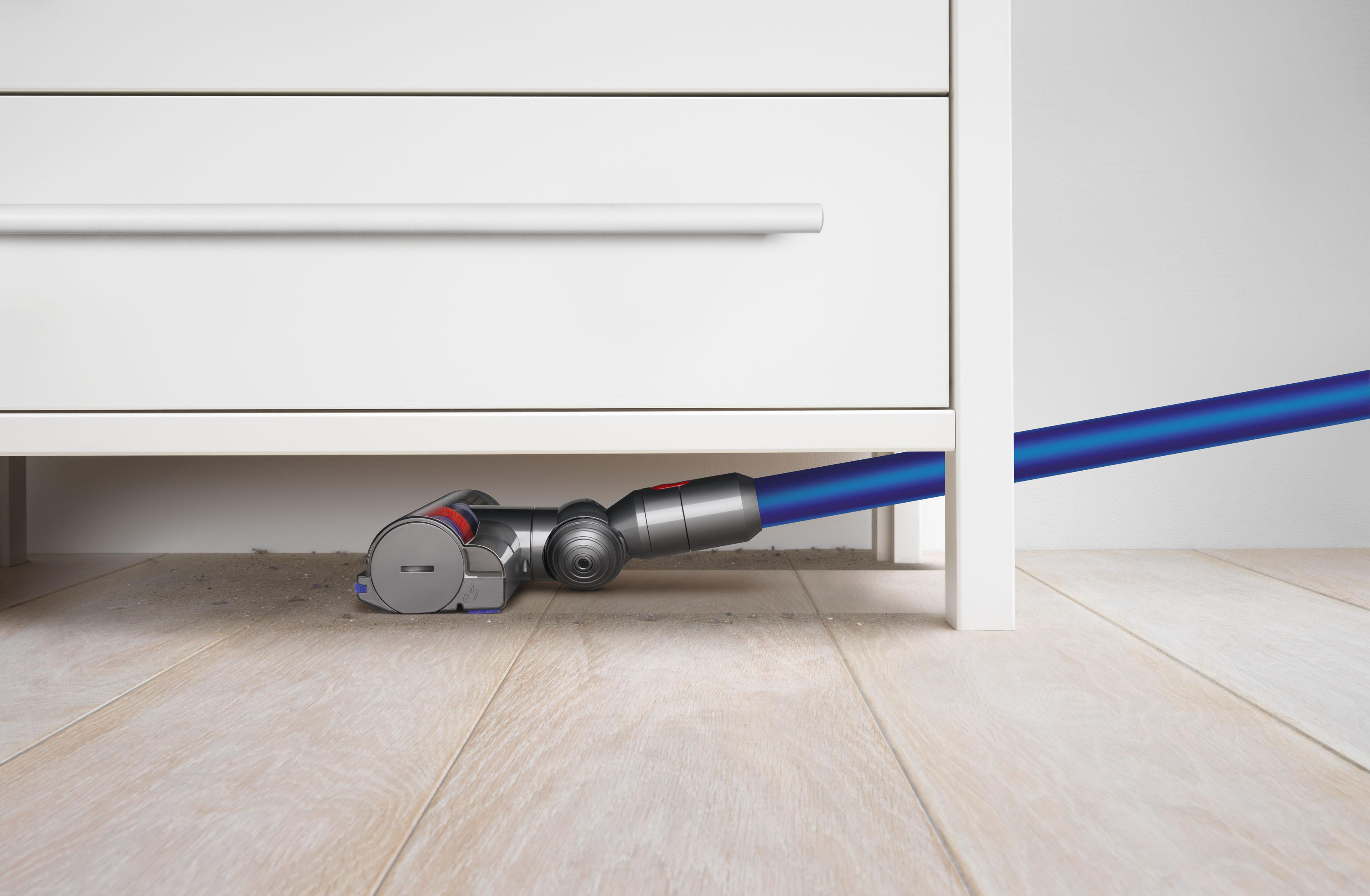 Staubsaugerkopf unter einem weißen Schrank, der einen Holzboden reinigt.