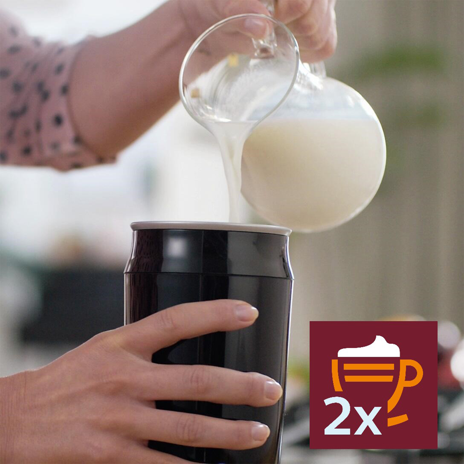 Persona che versa latte in una tazza termica nera. La tazza ha un'icona di schiuma accanto.