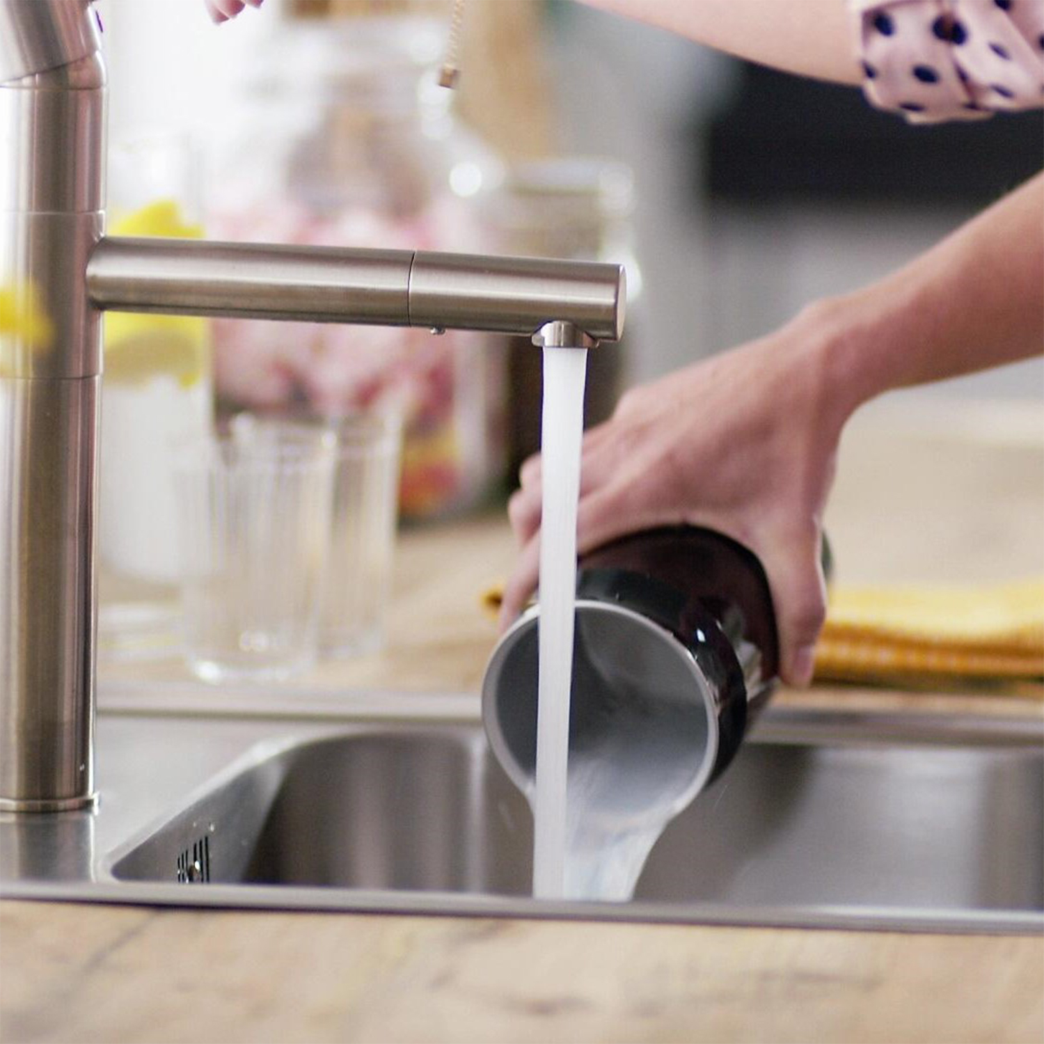 Una persona versa acqua da un rubinetto argentato in una tazza nera in un lavandino.