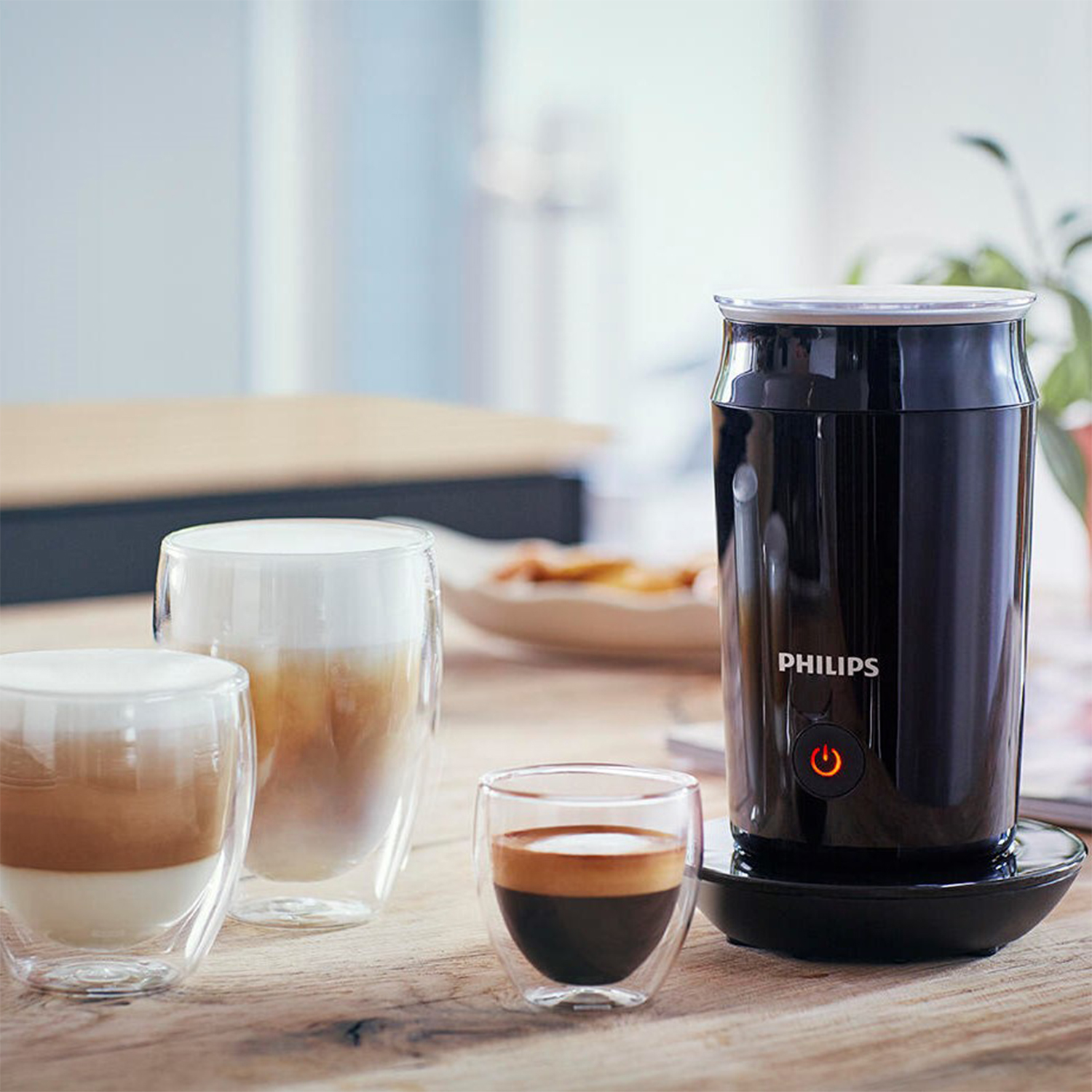 Un montalatte Philips nero con tre bicchieri di caffè, tra cui un latte e un espresso.