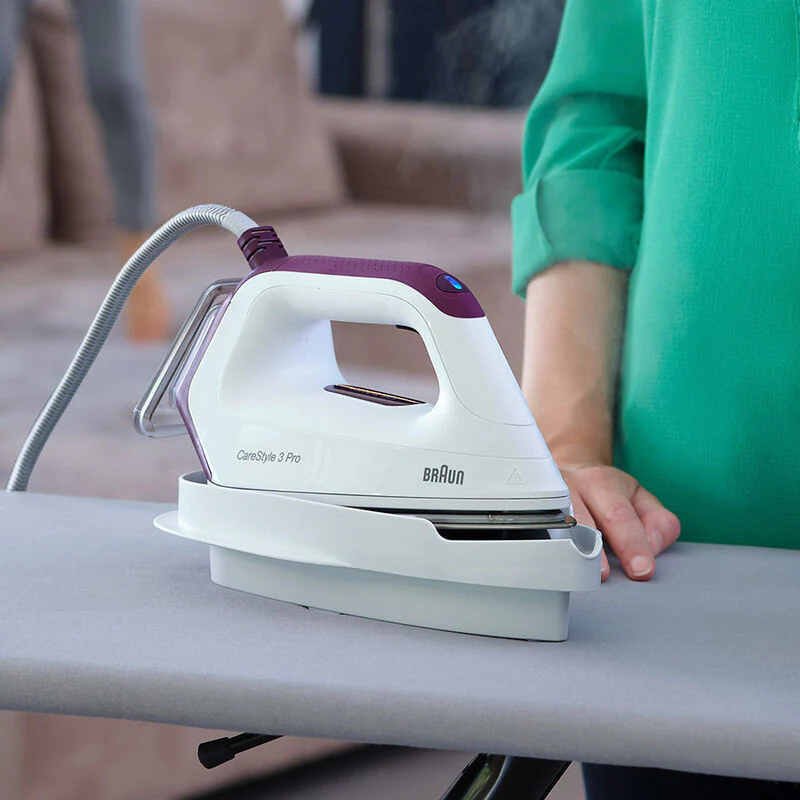 White and purple Braun iron on ironing board. Woman's hand on board.