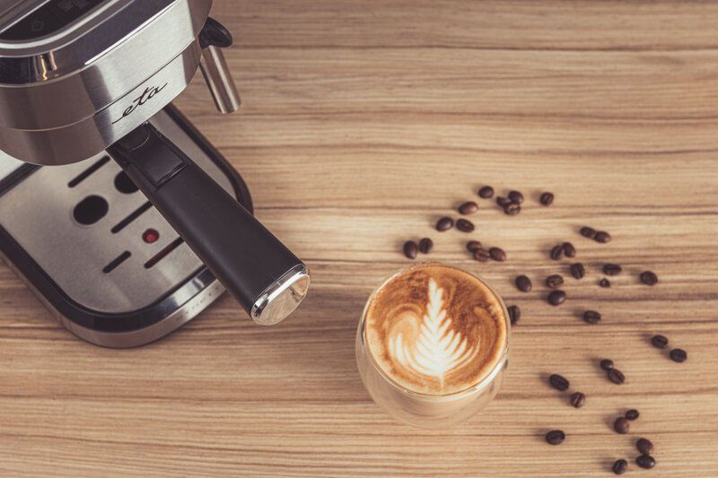 Kávé latte art-tal egy faasztalon, kávéfőzővel.