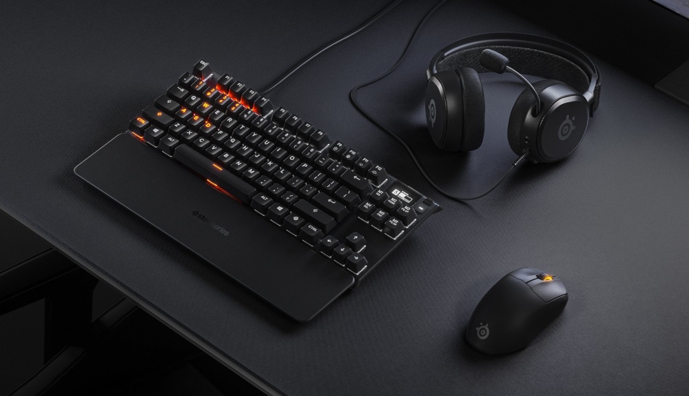 Clavier noir avec touches rétro-éclairées orange, casque et souris sur surface sombre.