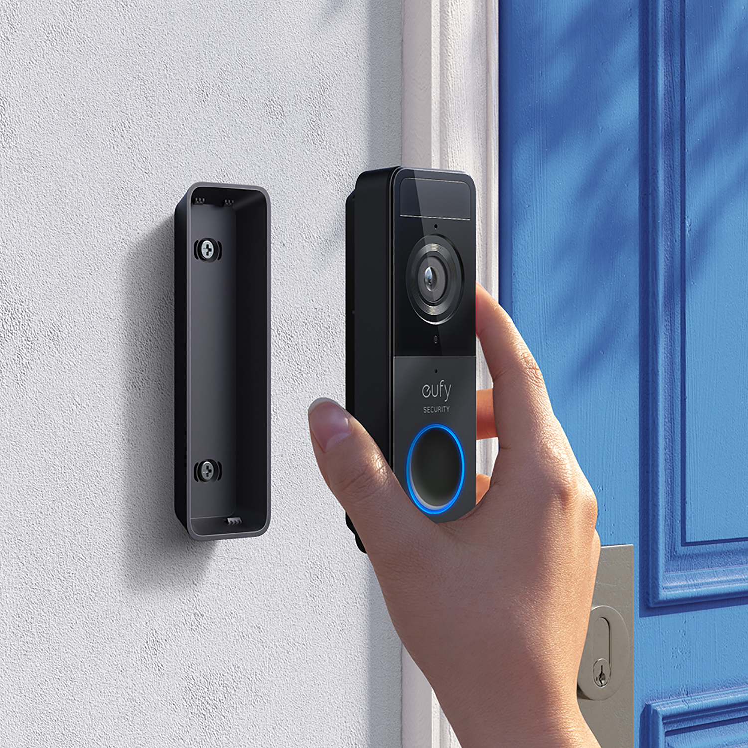 Hand installing a black doorbell on a white wall. Blue door in background.