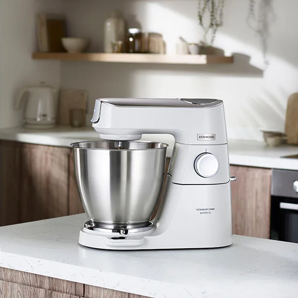 White stand mixer with a stainless steel bowl on a countertop, near a wooden cabinet.