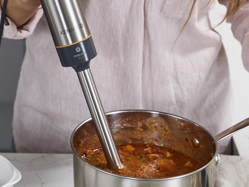 Hand using a Kenwood Triblade XL in a pot of tomato-based sauce.