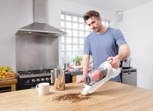 Un homme aspire du marc de café renversé d'une table en bois dans une cuisine.
