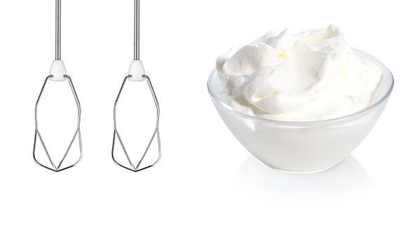 Zwei Schneebesen und eine Schüssel Schlagsahne auf weißem Hintergrund.
