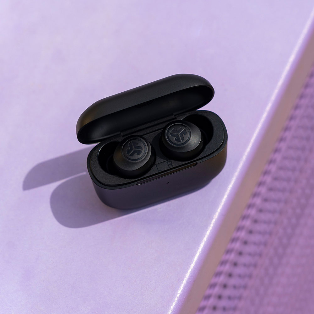 Un étui noir avec deux écouteurs sans fil noirs à l'intérieur, sur une surface violette.