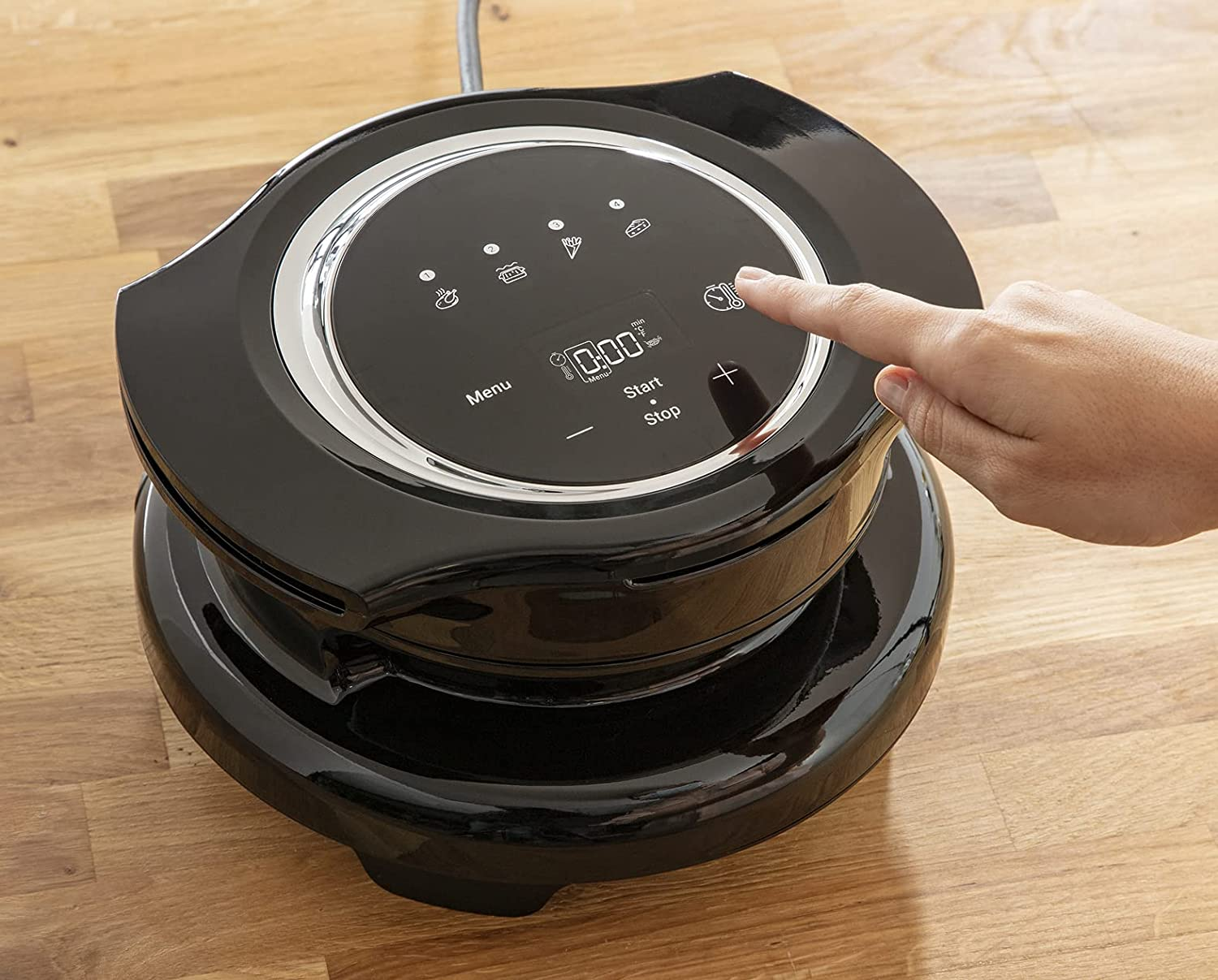 Black air fryer with a finger pointing at the button.