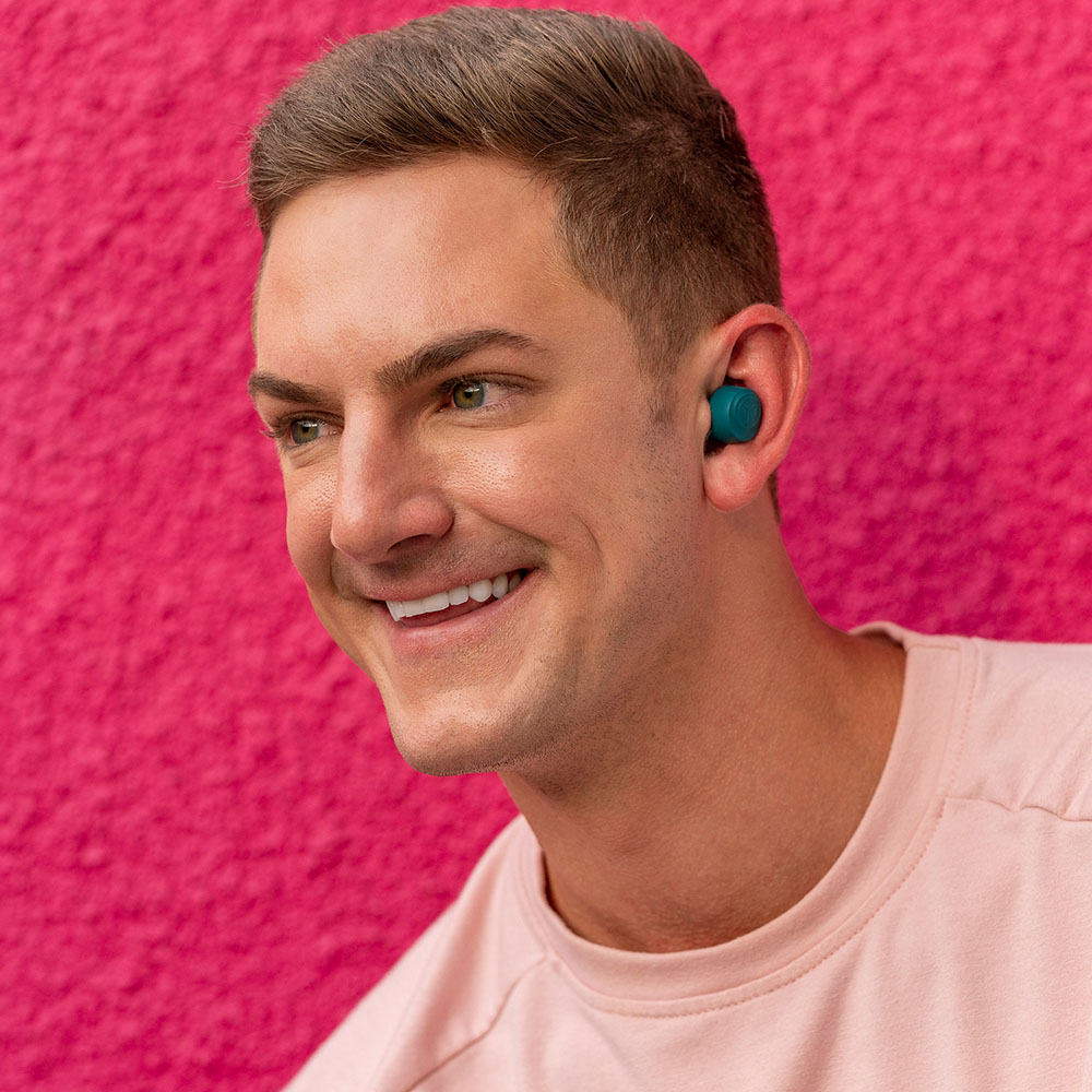 Uomo con auricolari turchesi sorride su sfondo rosa.
