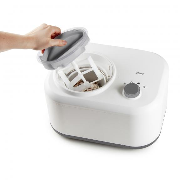 Witte ijsmachine met hand die deksel vasthoudt. Binnenkant met ijs en peddel.