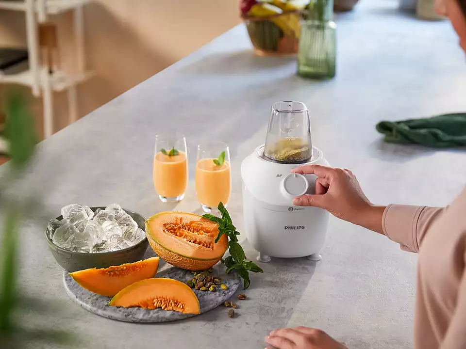 Egy személy egy fehér Philips turmixgépet használ gyümölccsel.