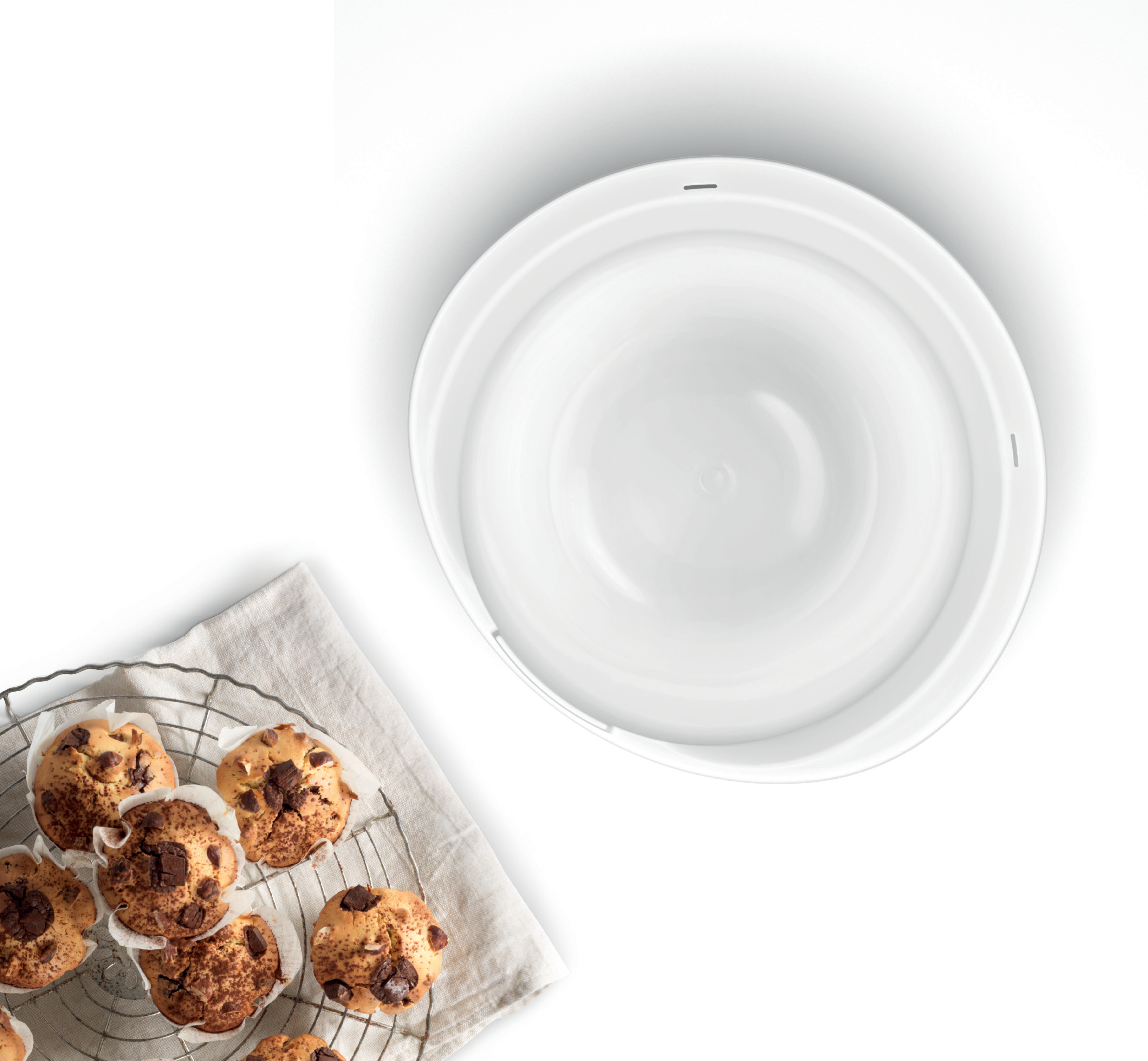 Muffins auf einem Drahtgestell neben einer großen weißen Schüssel, alles auf einer weißen Oberfläche.